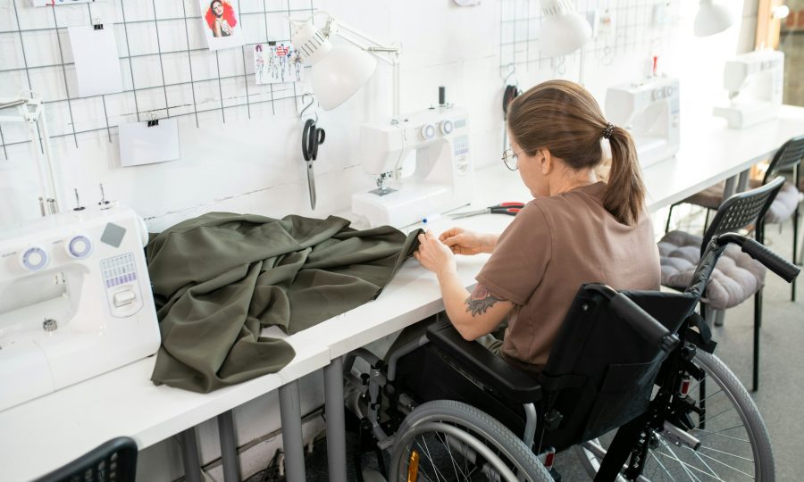 Young disable female in casualwear sitting in wheelchair by workplace inside contemporary workshop